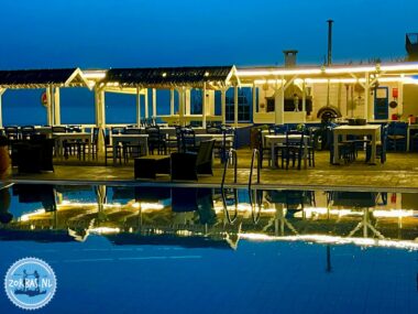 Beleuchteter Außenbereich einer Ferienanlage auf Kreta bei blauer Stunde mit einem Swimmingpool im Vordergrund, der die hellen Lichter der Bar und des Restaurants reflektiert.