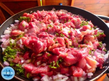 Zubereitung eines traditionellen Fleischgerichts mit Zwiebeln und frischen Kräutern während eines Kochworkshops mit Chef Helen auf Zorbas Island, Kreta.