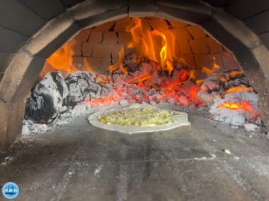 Ein traditioneller kretischer Steinofen mit lodernden Flammen und glühenden Kohlen, in dem ein frisches Fladenbrot gebacken wird. Ideal für authentische kulinarische Erlebnisse während eines Urlaubs auf Kreta im April.