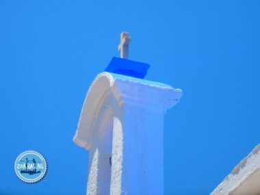 Nahaufnahme des Glockenturms einer typisch weiß getünchten griechischen Kapelle auf der Insel Dia vor der Küste von Kokkini Hani, Kreta, mit einem blauen Dachkreuz gegen einen strahlend blauen Himmel.