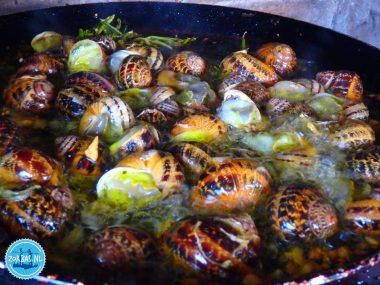 Pfanne mit brutzelnden kretischen Schnecken (Chochlioi), zubereitet in Olivenöl und Kräutern, während eines Kochworkshops auf Zorbas Island, Kreta.