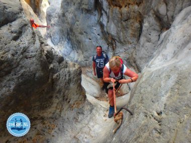 Wanderer klettern mit Unterstützung eines Seils und Metallbügels durch eine enge Felsspalte in der Kritsa-Schlucht bei Agios Nikolaos, Kreta.