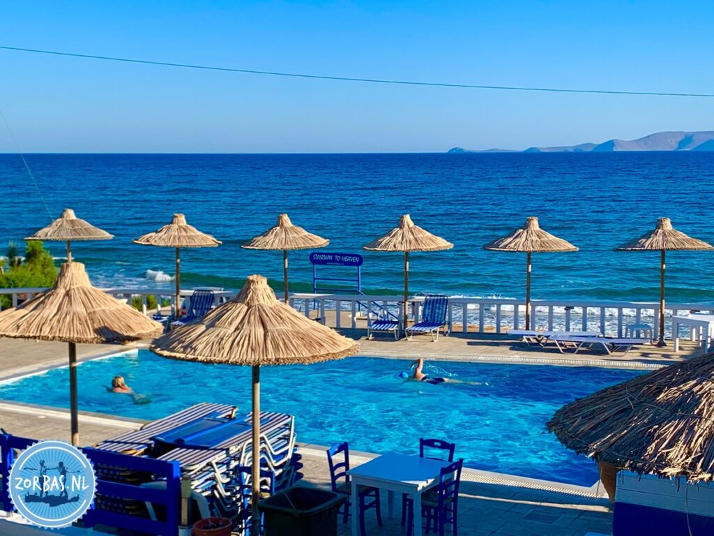 Ruhiger Sandstrand mit sanften Wellen und kristallklarem Wasser in Kokkini Hani auf Kreta, blauer Himmel und Inselblick am Horizont.