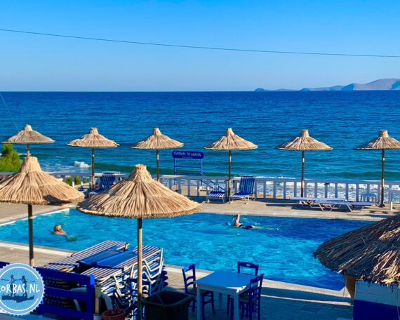 Ruhiger Sandstrand mit sanften Wellen und kristallklarem Wasser in Kokkini Hani auf Kreta, blauer Himmel und Inselblick am Horizont.