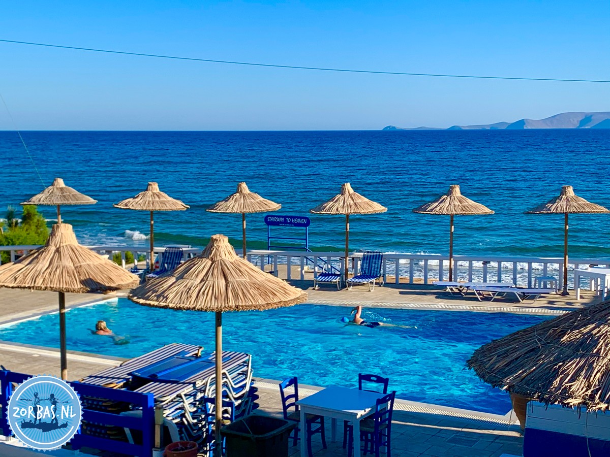 Ruhiger Sandstrand mit sanften Wellen und kristallklarem Wasser in Kokkini Hani auf Kreta, blauer Himmel und Inselblick am Horizont.