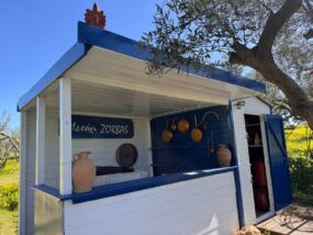 Authentische kretische Outdoor-Küche 'Metochi Zorbas' in Blau und Weiß mit traditionellen Tonkrügen unter einem Olivenbaum.