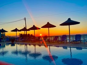 Malerischer Sonnenuntergang über einem Swimmingpool mit Silhouetten von Sonnenschirmen am Strand von Kokkini Hani, Kreta.